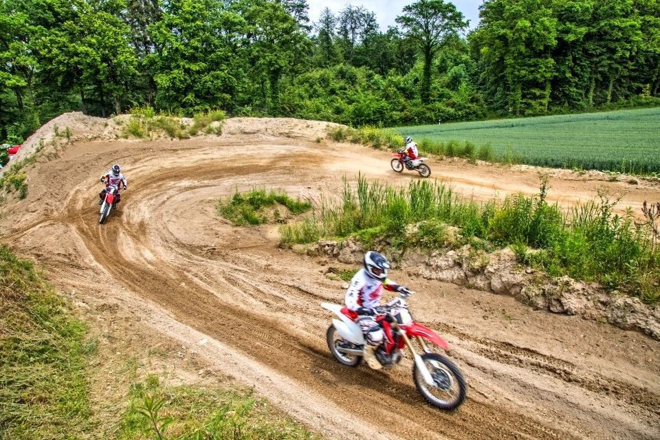 Motocross trip to Switzerland: riders on a curving sand track between green fields and woods